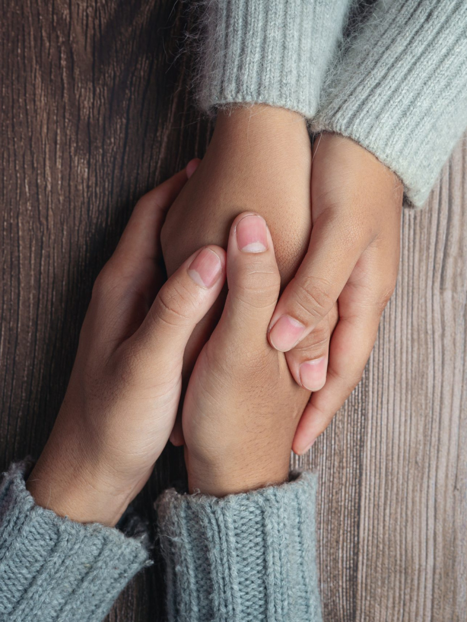 Two people holding hands together with love and warmth on wooden