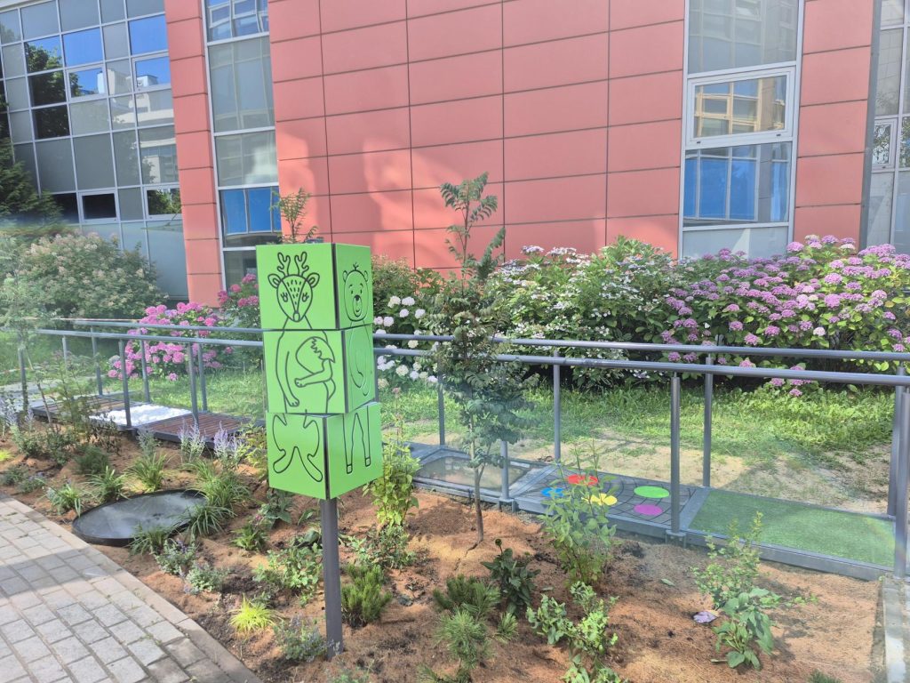 Nowe nasadzenia i zielona tablica edukacyjna w ogrodzie sensorycznym na terenie przyszpitalnym.